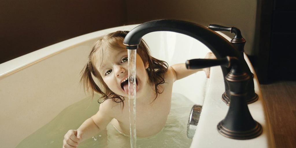 girl in bathtub tasting water from black faucet